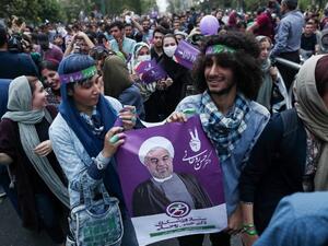 Supporters of newly re-elected Iranian President Hassan Rouhani hold a placard bearing a portrait of him as they take to the streets to celebrate his victory in downtown Tehran on May 20, 2017. (AFP/Behrouz Mehri)