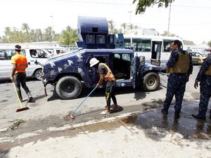 Iraqi workers clean the pavement as security forces stand guard at the site of a suicide bombing on July 24, 2016 near a checkpoint in the Kadhimiyah area, home to a major Shia shrine, in northern Baghdad. (AFP/Sabah Arar)