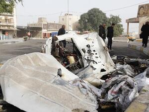 Iraqis walk past the wreckage of a vehicle in the aftermath of a bomb explosion in Baghdad's Al-Karkh district on December 4, 2016. (AFP/Sabah Arar)