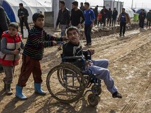 Children help a disabled young man at al-Khazer refugee camp near the Kurdish checkpoint of Aski kalak, 40 km West of Erbil on December 21, 2016. (AFP/JM Lopez)