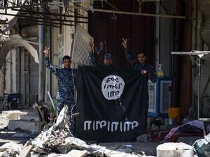 Iraqi government forces flash the sign for victory while holding a Daesh flag in western Mosul's Zanjili neighbourhood on June 9, 2017, during ongoing battles to try to take the city from Islamic State (IS) group fighters. (Mohamed El-Shahed/AFP)