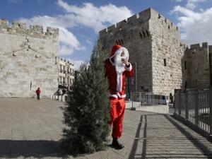 Issa Kassissieh, dressed as Santa Claus, carries a Christmas tree outside the Jaffa Gate in Jerusalem. [mondoweiss]