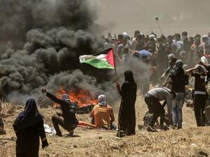 A Palestinian woman holding her national flag looks at clashes with Israeli forces near the border between the Gaza strip and Israel east of Gaza City on May 14, 2018. (MAHMUD HAMS/ AFP)