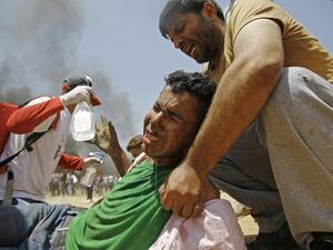 A Palestinian man assists a wounded protestor during clashes with Israeli security forces near the border between Israel and the Gaza Strip/AFP