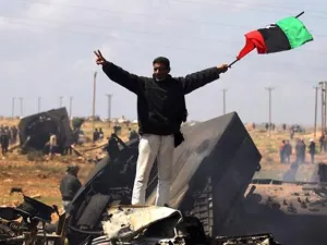 ليبي يرفع علم المعارضة على حطام آليات جيش القذافي