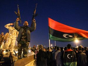 A Libyan man points two Kalashnikov assault rifles in the air as a national flag waves behind him during a celebration marking the sixth anniversary of the Libyan revolution. (AFP/File)