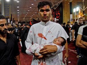 Young participant: A man holds a baby during an Ashura cutting ceremony, which sees male Shiite Muslims self-flagellate to commemorate the death of Imam Hussein, the grandson of the Prophet Muhammad, on the battlefield (AFP)
