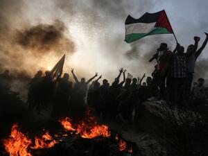 Palestinian protesters wave national flags as they stand near burning tyres during a demonstration on the beach near the maritime border with Israel. (MAHMUD HAMS / AFP)