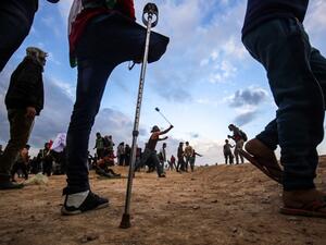 A Palestinian amputee stands by as others protest and use slingshots to hurl objects during clashes following a demonstration along the border with Israel. (SAID KHATIB / AFP)