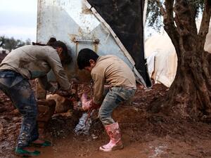 A Syrian boy and girl wash their boots and shoes from a cistern at a camp for the displaced near the village of Shamarin, near the border with Turkey. (AFP)