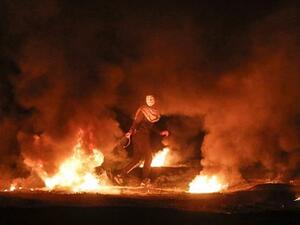 A masked Palestinian demonstrator pulls a burning tire during a night demonstration near the fence along the border with Israel, east of Gaza City, on February 11, 2019. (AFP/ File)