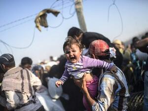 A man carries his child across the border (BULENT KILIC/AFP)