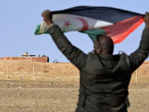 A Saharawi holds up a Polisario Front flag in Al-Mahbes area near Moroccan soldiers guarding the wall separating the Polisario-controlled Western Sahara from Morocco. (AFP Photo/STRINGER)