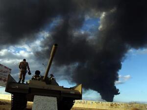 A member of the Libyan army stands on a tank as heavy black smoke rises from the city's port during clashes against Islamist gunmen in the eastern Libyan city of Benghazi on December 23, 2014. (AFP/Abdullah Doma)