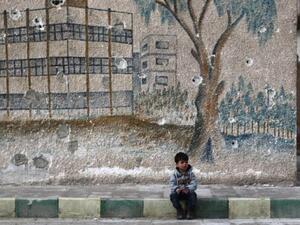 A Syrian child sits in front of a mural covered in bullet holes on the wall. (AFP/File)