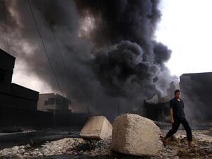 An Iraqi man walks near smoke billowing from oil wells, set ablaze by Daesh militants before fleeing the oil-producing region of Qayyarah, on August 30, 2016. (AFP/File)