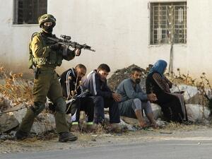 Israeli soldier keeps watch as Palestinians sit after the army entered Yatta earlier this week. (AFP/File)
