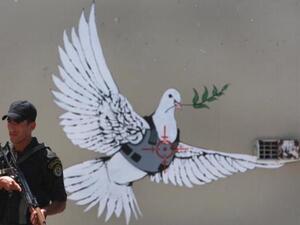 An Israeli solider stands by iconic Banksy grafitti on the Israeli separation barrier that runs through Bethlehem. Getty Photo  An Israeli solider stands by iconic Banksy grafitti on the Israeli separation barrier that runs through Bethlehem. Getty Photo