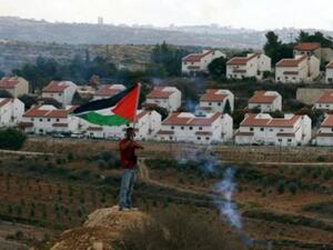 فلسطيني يحمل علما فلسطينيا مقابل مستوطنة يهودية في الضفة الغربية المحتلة
