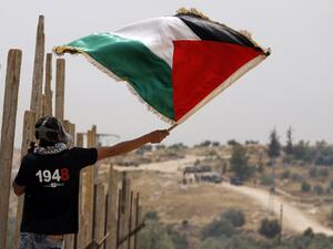 A Palestinian protester, wearing a gas mask, waves a Palestinian flag in front of Israeli security forces on May 13, 2016 in the West Bank village of Bilin, near Ramallah, during a march against the building of Israel's controversial separation barrier and the construction of Israel settlements. (AFP/Abbas Momani)