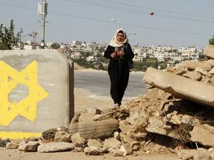 A Palestinian woman passes a roadblock, on which a star of David is painted, on July 10, 2016 in the West Bank village of Sair, east of Hebron, as the IDF keeps the area under lockdown after an Israeli man was shot and wounded near the Tekoa settlement. (AFP/Hazem Bader)