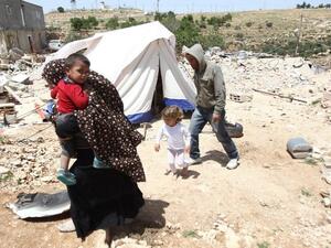 A Palestinian family, whose house was demolished by Israeli bulldozers, walk past a tent on April 21, 2015 in the southern West Bank. (AFP/File) 