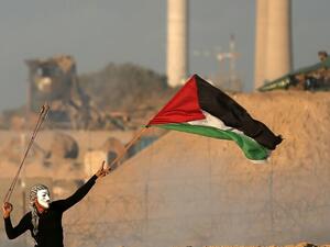 A masked Palestinian protester carries a national flag as he hurls stones during a demonstration calling for an end to the Israeli blockade on Gaza. (MAHMUD HAMS / AFP)