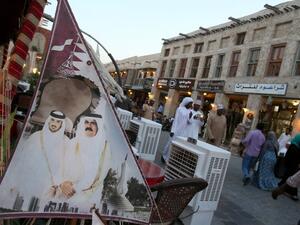 This file photo taken on June 25, 2014 shows people walking past a banner bearing portraits of former emir of Qatar Sheikh Hamad bin Khalifa al-Thani (R) and his son current leader Sheikh Tamim bin Hamad al-Thani displayed at Souq Waqif in the Qatari capital Doha. (Karim Jaafar/AFP)