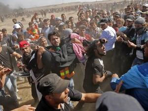 Palestinians carry a demonstrator injured during clashes with Israeli forces near the border between the Gaza strip and Israel east of Gaza City on May 14, 2018/AFP