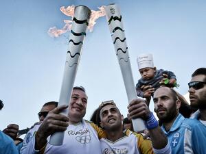 President of the Hellenic Olympic Committee Spyros Kapralos (L) hands over the Olympic Flame to Syrian refugee Ibrahim al-Hussein (C), 27, an amputee swimmer
LOUISA GOULIAMAKI / AFP