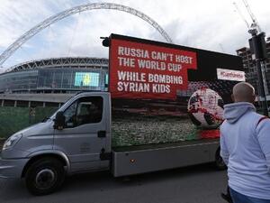 A mobile billboard showing a design of a blood-stained football on a pitch, with the words "Russia can’t host the World Cup while bombing Syrian kids", is driven past Wembley Stadium ahead of the International friendly football match between England and Italy in London on March 27, 2018.
Ian KINGTON / AFP