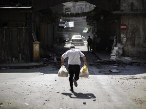 A Syrian man carrying grocery bags tries to dodge sniper fire as he runs through an alley near a checkpoint manned by the Free Syria Army in Aleppo. (AFP/Marco Longari)