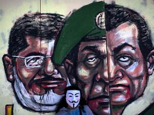 Egyptian protester wears a Guy Fawkes mask while posing for a photo next to a mural painted overnight on the exterior wall of the presidential palace depicting president Mohammed Morsi, left, former military council ruler Hussein Tantawi, center and ousted President Mubarak with Arabic that reads "No, the brotherhood's constitution is not valid, in Cairo. [AP Photo/Nasser Nasser