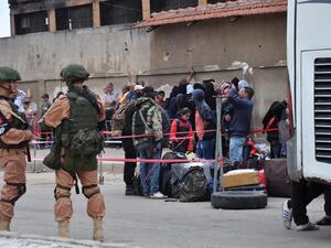 Russian troops (L) stand guard as Syrian opposition fighters and their families board a bus at a checkpoint manned by regime forces ahead of their evacuation on May 20, 2017. (Stringer/AFP)