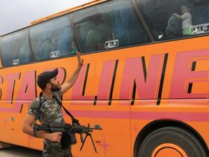 A rebel fighter waves at civilian arriving by bus in al-Bab, in the northern province of Aleppo, after leaving al-Waer, the last opposition-held neighborhood of the central city of Homs, on May 5, 2017. (AFP/Zein Al Rifai)