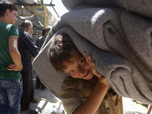 A child in the Syrian town of Douma in the Eastern Ghouta region near Damascus carries blankets distributed by relief workers and the United Nations on July 26, 2018 (AFP/File)