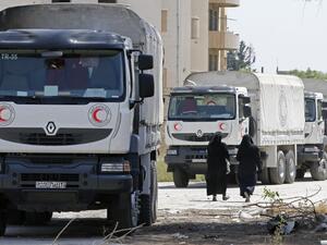 Women walk by Syrian Red Crescent vehicles in Damascus' north eastern al-Qaboun suburb on May 16, 2017, after the formerly rebel-held neighbourhood was retaken by Syrian government forces. (AFP/Louai Beshara)