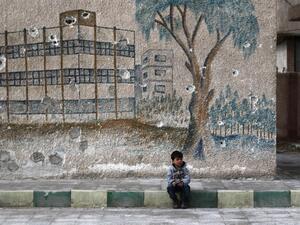 A Syrian child sits in front of a mural covered in bullet holes in Eastern Ghouta, on the outskirts of Damascus. (AFP/Abdulmonam Eassa)