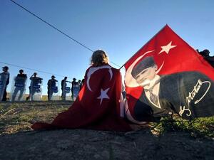 TURKEY, Silivri : Wrapped in a Turkish flag and holding another one with a portrait of Mustafa Kemal Ataturk, a protestor sits in front of police forces blocking the access to a courthouse in Silivri, near Istanbul, on August 5, 2013, where Ilker Basbug was sentenced to life imprisonment. AFP PHOTO / OZAN KOSE