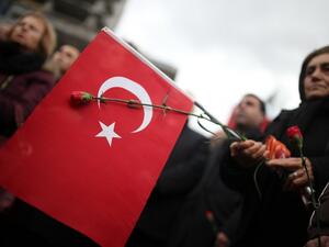 A woman holds a red carnation and a Turkish flag during the funeral ceremony of Turkish police officer Fethi Sekin and courthouse officer Musa Can, who were killed in a car bombing on January 5, in Izmir on January 6, 2017. (AFP/Stringer)
