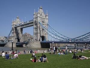 People relax in the hot and sunny weather on the grass beside Tower Bridge and the river Thames in London on May 26, 2017. (DANIEL LEAL-OLIVAS / AFP)