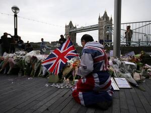 A man holds a Union flag as he kneels near flowers layed at Potters Fields Park in London on June 5, 2017, during a vigil to commemorate the victims of the terror attack on London Bridge and at Borough Market that killed seven people on June 3. (AFP/Daniel Leal-Olivas)