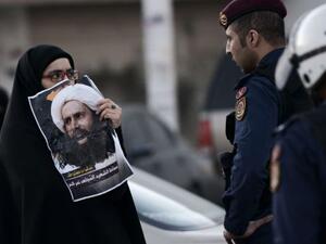 A woman holds a picture of the executed Shia cleric Nimr al-Nimr infront of a Saudi policeman during a protest. (AFP/File)