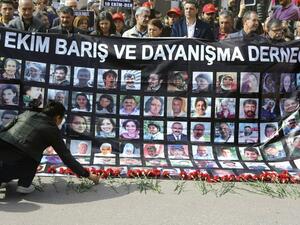 A wonam lays red carnations as people hold a banner with pictures of victims of October 10 bombings during a memorial ceremony in Ankara on April 10, 2016. (AFP/Adem Altan)
