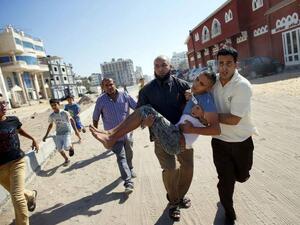 A Palestinian carries a wounded boy following an Israeli military strike (AFP/File Photo)