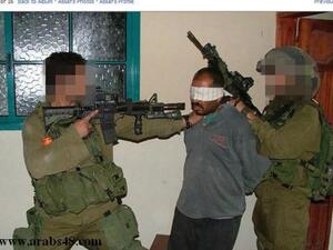 صورة لجندي اسرائيلي يوجه بندقيته الى وجه فلسطيني مكبل ومعصوب العينين داخل منزله في غزة