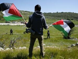 A Palestinian man holds two flags as he overlooks farmland in Gaza. (AFP/File)