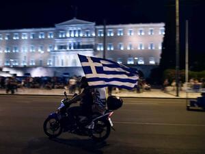 A motorcylist with his passenger holding a Greek flag passes in front of the Greek Parliament (AFP/File Photo)	