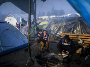 Children sit by a bonfire as a man cooks at the migrants and refugees makeshift camp at the northern village of Idomeni, at the Greek-Macedonian border, on April 5, 2016. (AFP/Bulent Kilic)