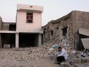 A man squats outside his destroyed home in Shonbeh, near Bushehr (AFP)